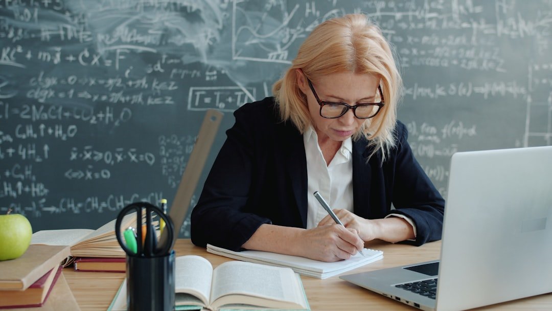 a teacher marking papers beside an open laptop