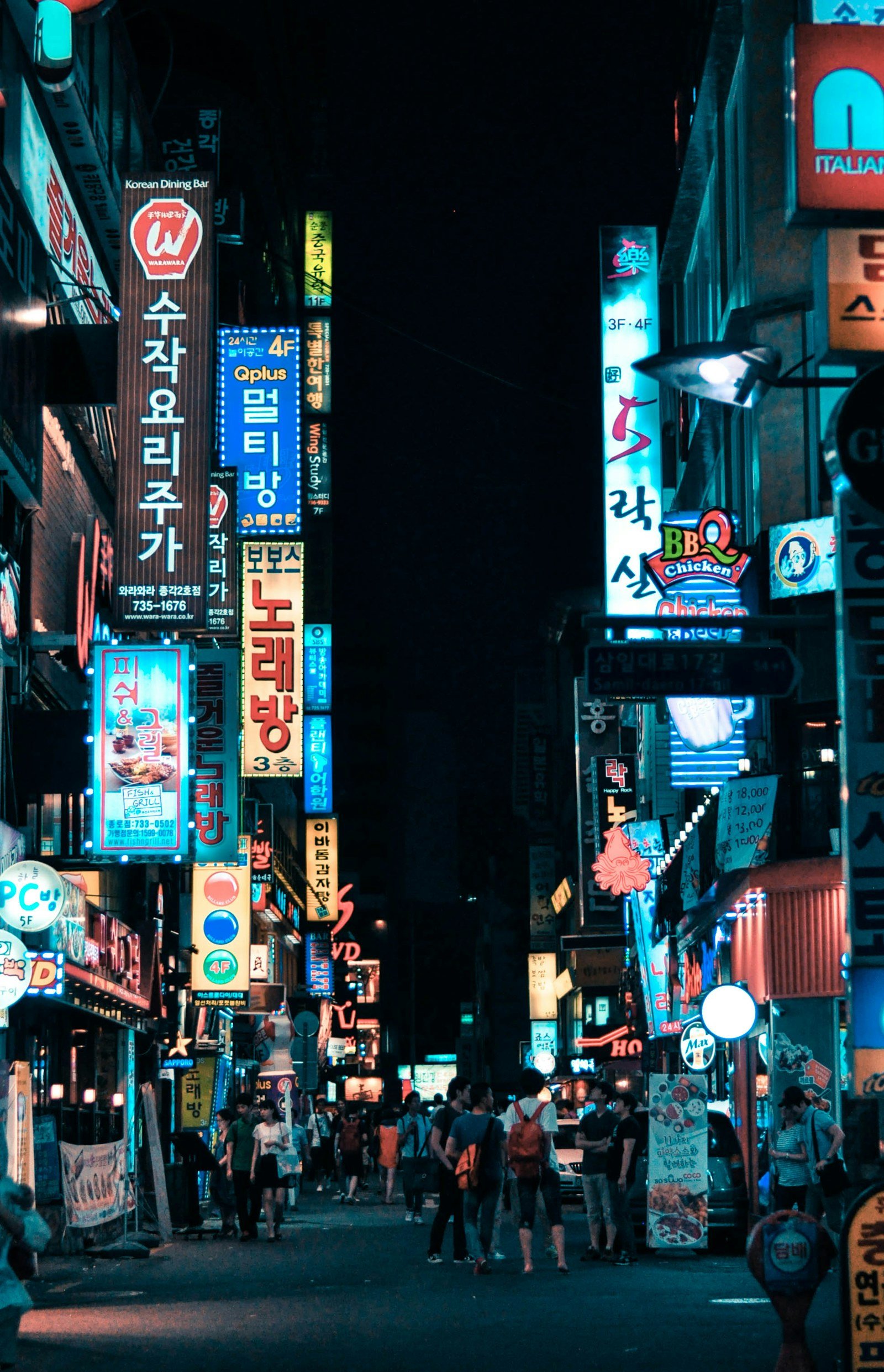 a Seoul street at night lined with glowing Korean neon signs