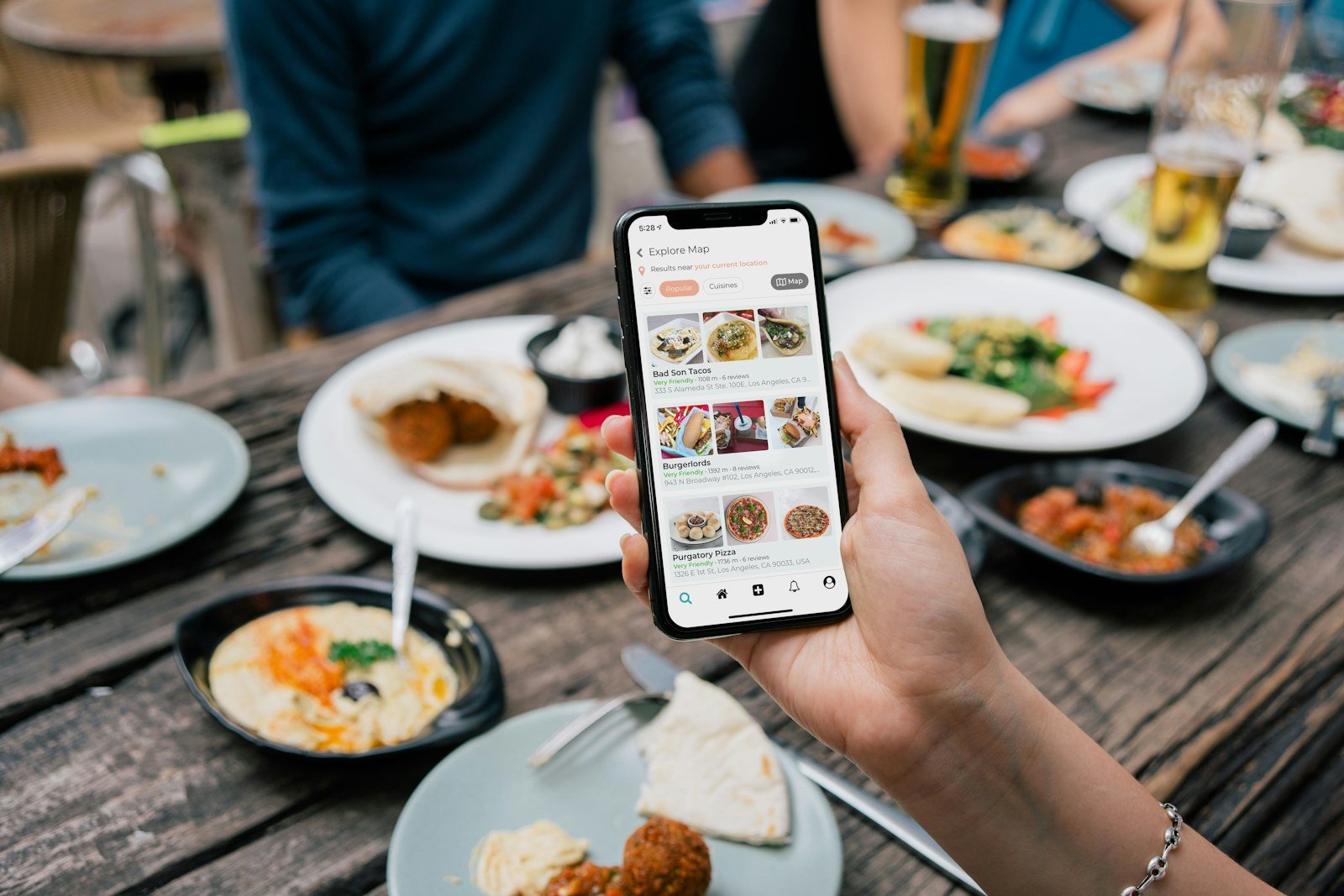 a hand holding a phone showing a food ordering app above a table of dishes