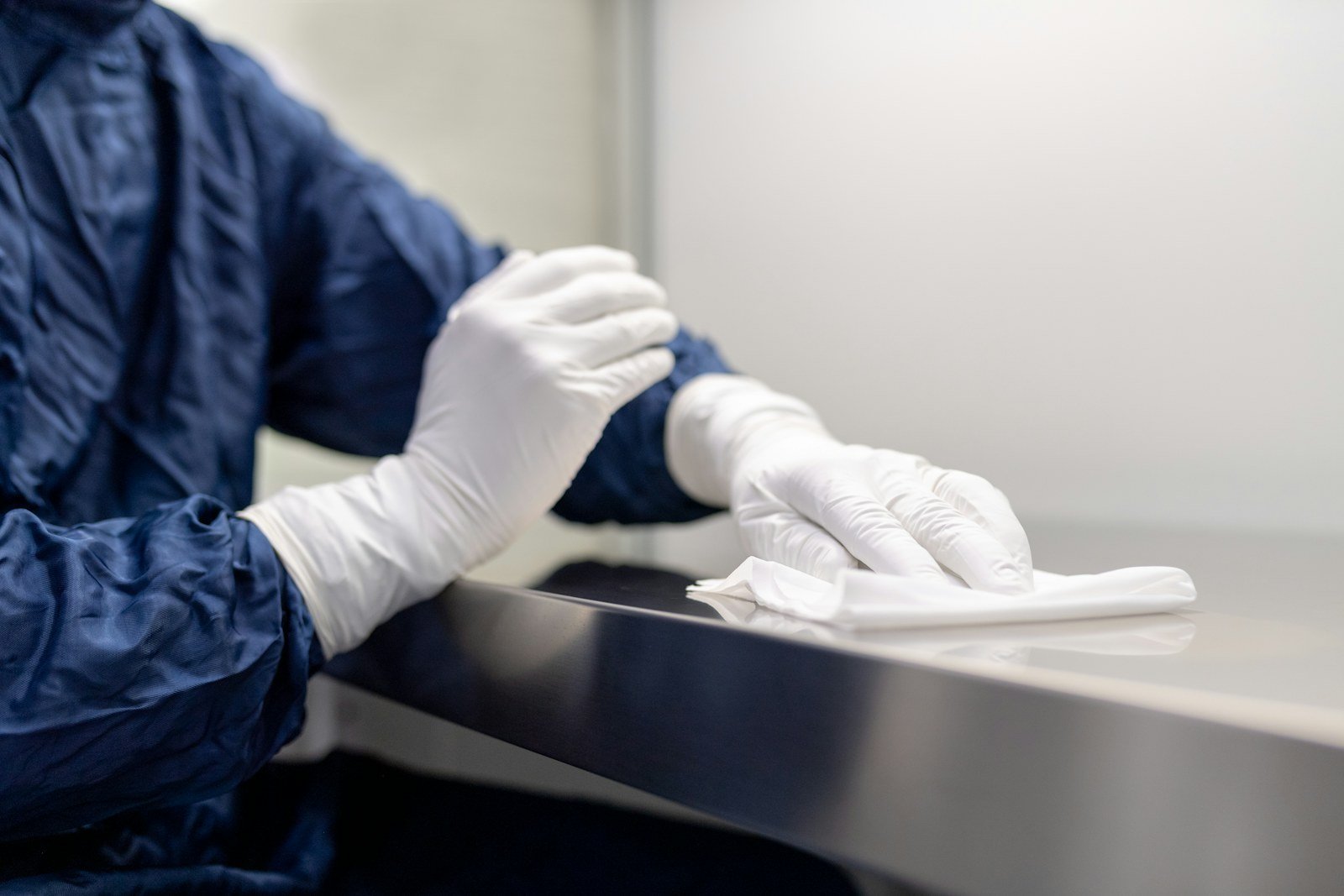 a worker in cleanroom gown and gloves wiping a surface in a manufacturing facility