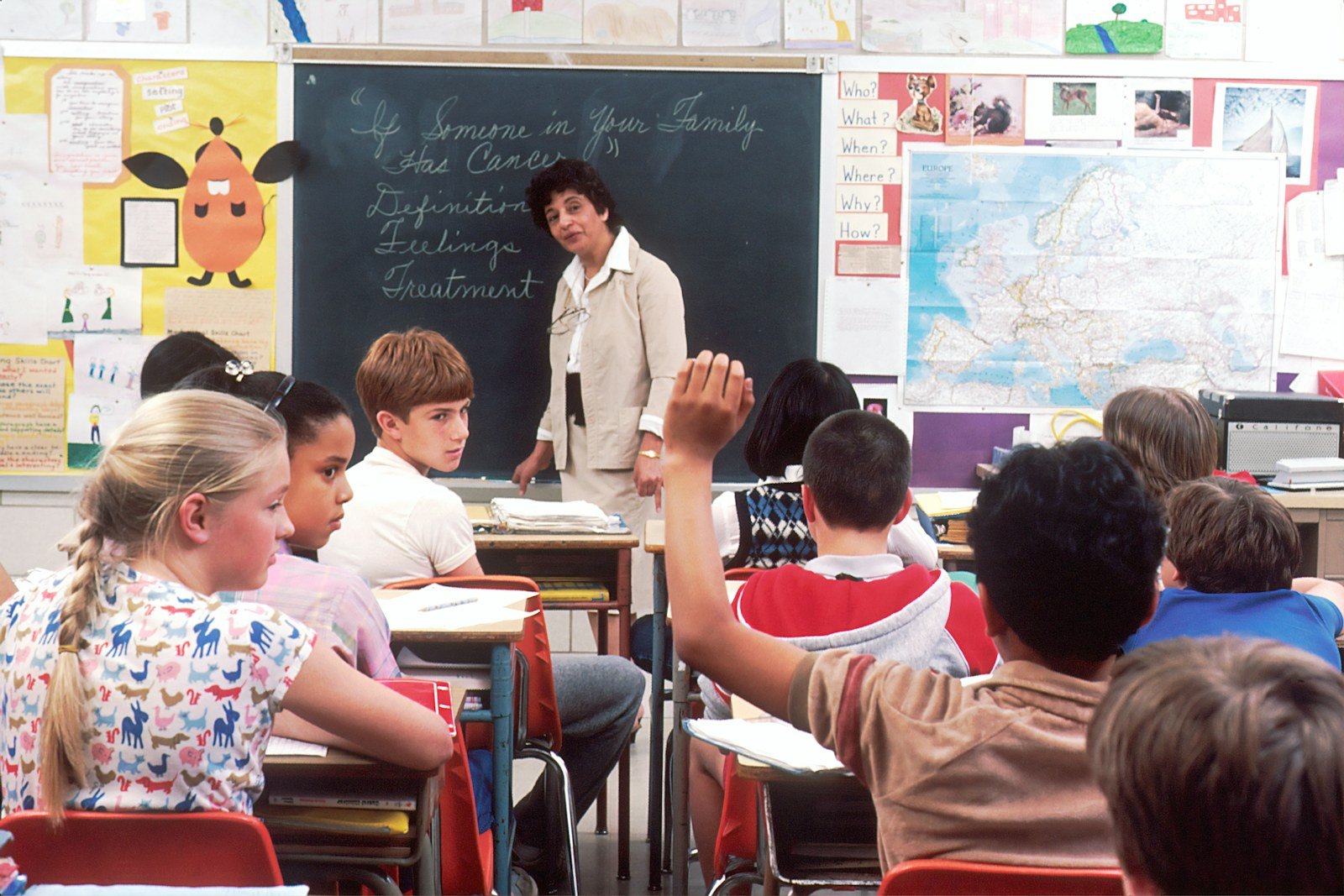 a teacher at the blackboard with students raising hands