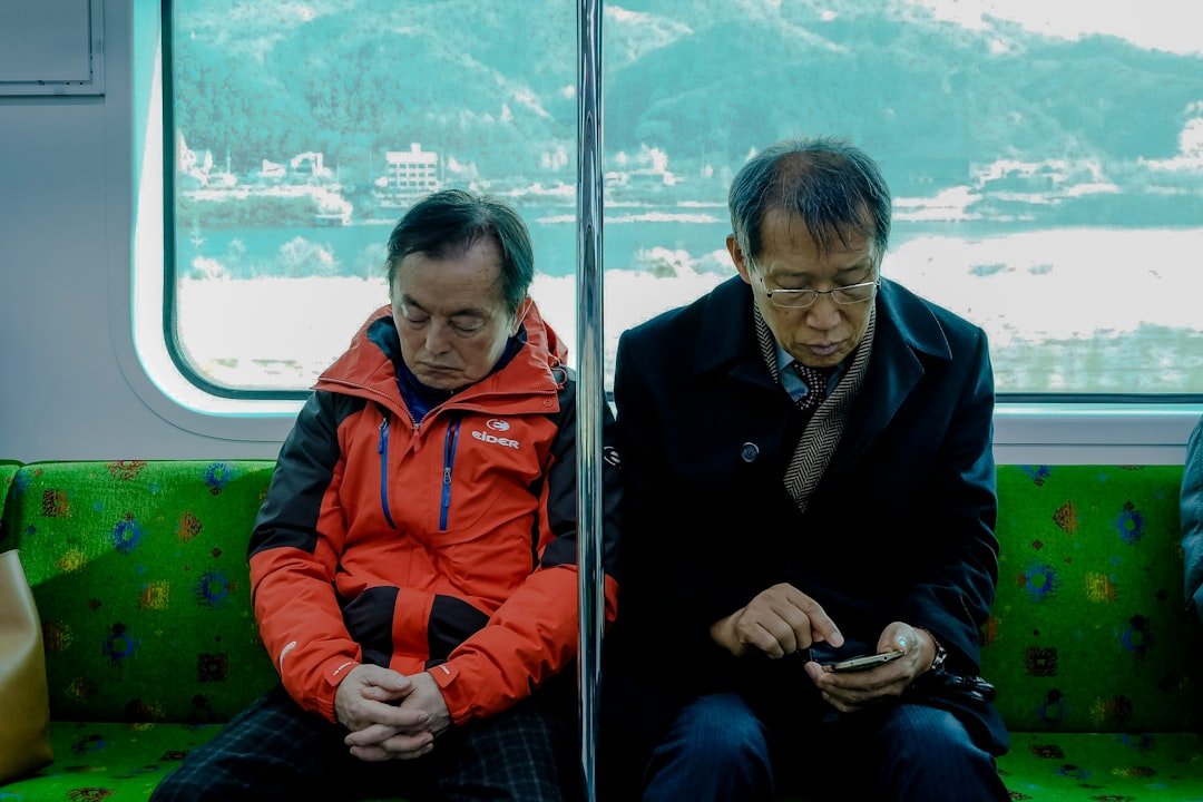 two older commuters on a Korean train, one using KakaoTalk on his phone